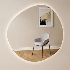 a chair sitting in front of a white wall with a framed painting on the wall