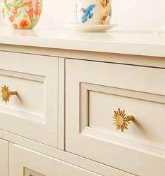 a white dresser with gold handles and knobs next to a flower vase on top