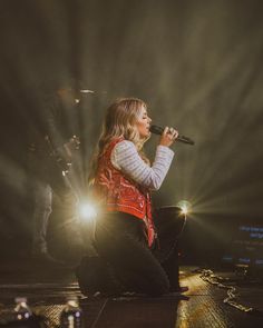 a woman sitting on the ground while holding a microphone in her hand and singing into a mic