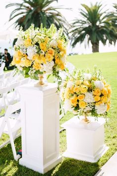 yellow and white flowers are placed on pedestals at the end of an outdoor ceremony