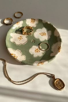 a green plate with white flowers on it and two gold rings laying next to it