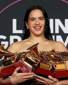 a woman holding two awards in her hands and smiling at the camera while wearing a gold dress