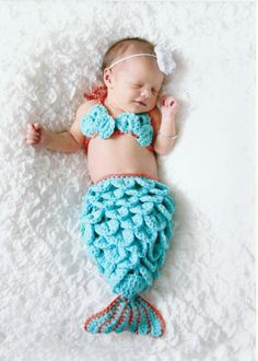 a baby wearing a blue crochet mermaid tail and diaper laying on the floor