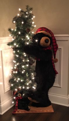 a teddy bear standing on its hind legs next to a christmas tree decorated with lights