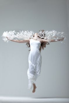 a woman in white dress flying through the air with feathers on her head and arms