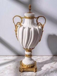 a white and gold vase sitting on top of a marble table next to a wall