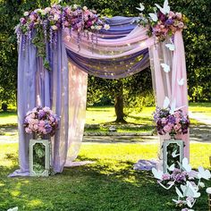 an outdoor wedding ceremony setup with purple and pink flowers on the arch, white lanterns and butterfly decorations