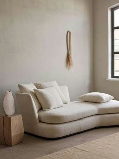 a white couch sitting in front of a window next to a vase and pillow on the floor