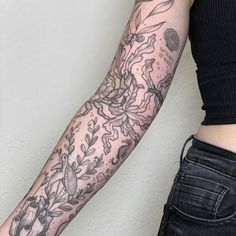 a woman's arm with tattoos on it and flowers in the middle, next to a white wall