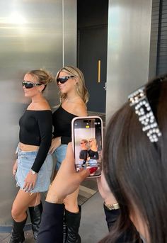 two women in short shorts and black top taking a selfie with their cell phone