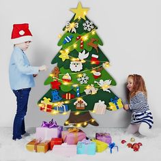 two children decorating a christmas tree with lights and presents on the floor in front of them