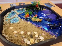 an ocean themed sand tray with rocks, shells and seaweed in it on a table