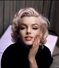 a woman with blonde hair and orange nail polish posing for a photo in front of a white table