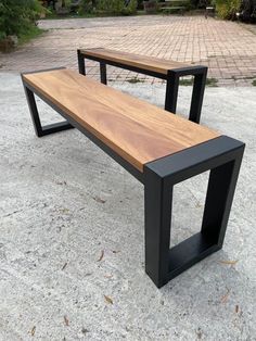 two wooden benches sitting next to each other on top of a cement ground with trees in the background