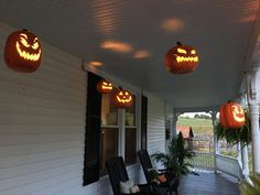 three pumpkins are lit up on the front porch for halloween time, with jack - o'- lanterns hanging from the ceiling