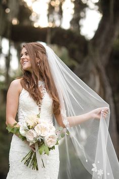 a woman in a wedding dress holding a veil over her head and smiling at the camera