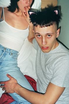 a man and woman laying in bed with cat ears on their head, one is holding the other's belly