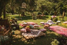 an outdoor picnic area with lots of pillows and blankets on the grass, in front of a tree