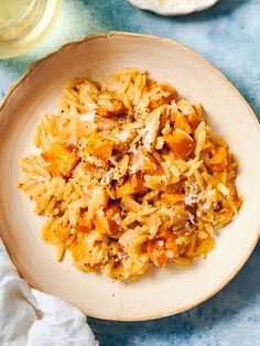 a white bowl filled with pasta and meat on top of a blue table cloth next to a glass of water