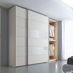 an open closet with clothes on hangers in a room next to a bed and window