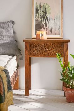 a wooden table sitting next to a bed with a plant on it's side