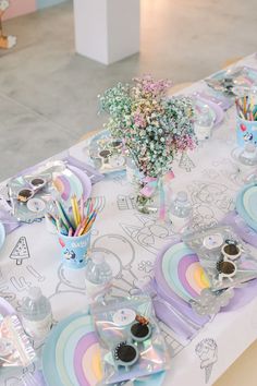 the table is set for a child's birthday party with pastel colors and decorations