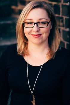 a woman wearing glasses standing in front of a brick wall with a necklace on her neck