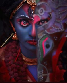 a woman with blue face paint on her face and red feathers around her neck, behind a curtain