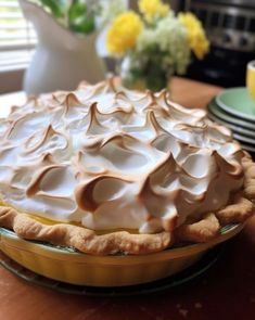 a pie sitting on top of a wooden table next to plates and cups with yellow flowers in the background