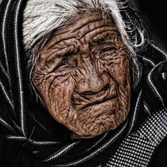 an old woman with wrinkles on her face and scarf around her neck is looking at the camera