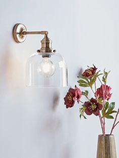 a glass vase with flowers in it next to a wall light