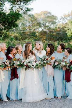 a group of women standing next to each other in blue dresses and holding bouquets