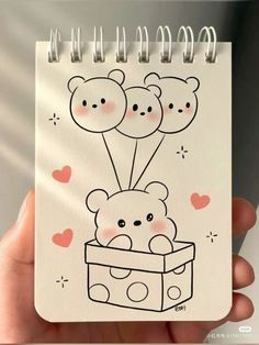 a hand holding a notebook with a drawing of a teddy bear in a box