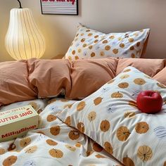 an apple sits on top of a bed with orange sheets and pillow cases in front of a lamp