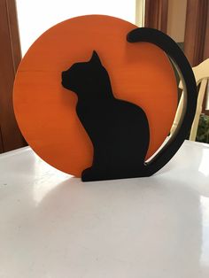 a black cat sitting on top of an orange circle shaped sign with the shape of a cat's head