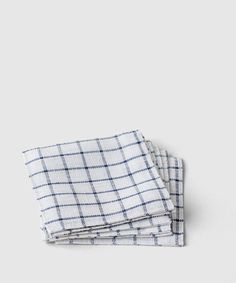 three white and blue checkered napkins stacked on top of each other in front of a gray background