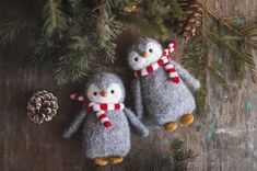 two small stuffed penguins are hanging from a christmas tree with pine cones and evergreen needles