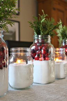 four jars filled with candles sitting on top of a table covered in snow and greenery