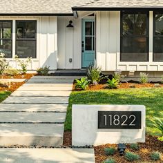 a white house with a blue front door and number on the sidewalk in front of it