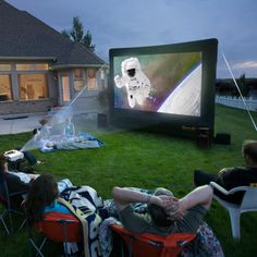 people sitting in lawn chairs watching an outdoor movie on the big screen at night time