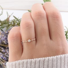 a woman's hand with a gold ring on it and flowers in the background