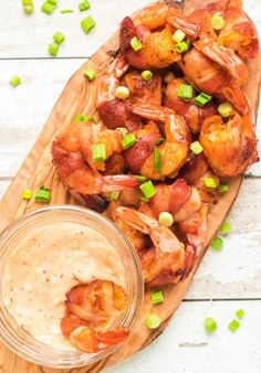 a wooden platter filled with shrimp next to a bowl of ranch sauce and green onions