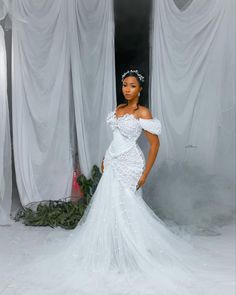 a woman in a white wedding dress standing next to a curtained wall with flowers on it