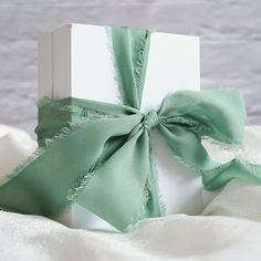 a white box with a green ribbon tied around it on top of a bed sheet