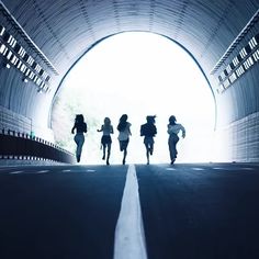 four people are running through a tunnel on a road with the light at the end