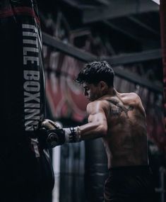 a man with no shirt on standing in a boxing ring holding a punching bag and looking at the camera