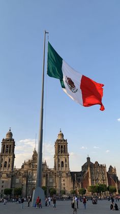 the mexican flag is flying in front of an old building with many people walking around