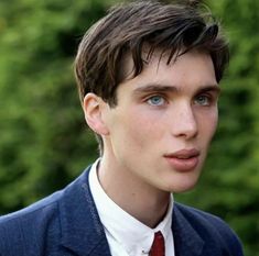 a man in a suit and tie looking off into the distance with trees behind him