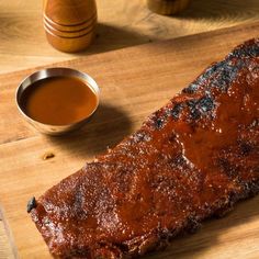 a piece of meat is sitting on a cutting board next to some dipping sauces