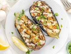 two stuffed eggplant halves on a white plate with lemon wedges and parsley